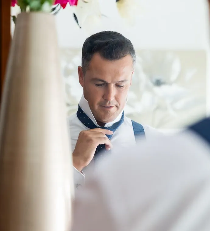 Ezequiel colocándose la corbata fremte a un espejo. Fotografía de bodas en Sevilla.